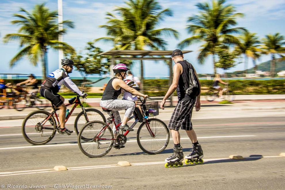 Imagem de uma família de bicicleta e um rapaz andando de patins na avenida da Praia de Cambori.